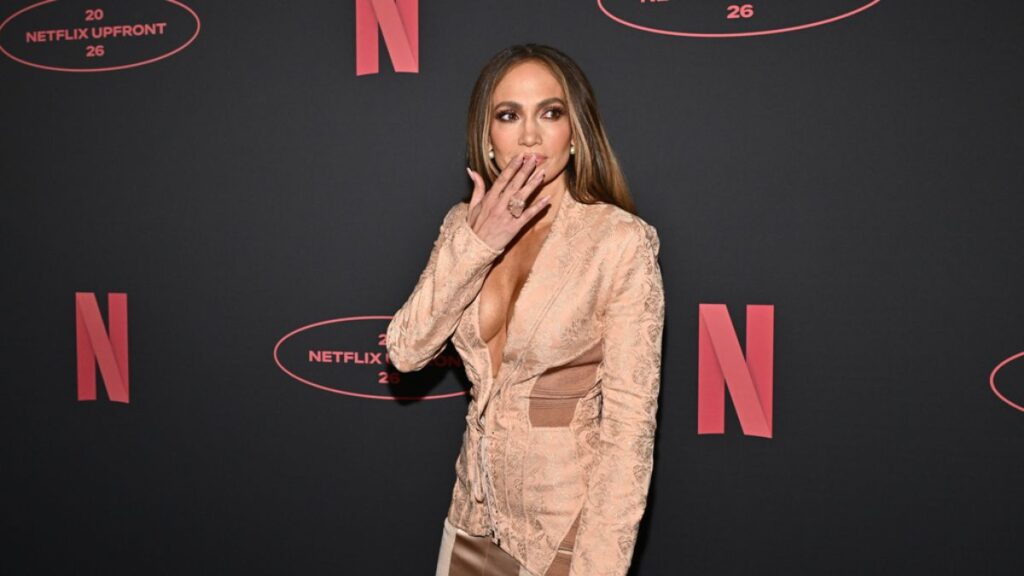 Jennifer Lopez sonriendo mientras ve una escena romántica de Off Campus en su pantalla