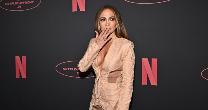 Jennifer Lopez sonriendo mientras ve una escena romántica de Off Campus en su pantalla