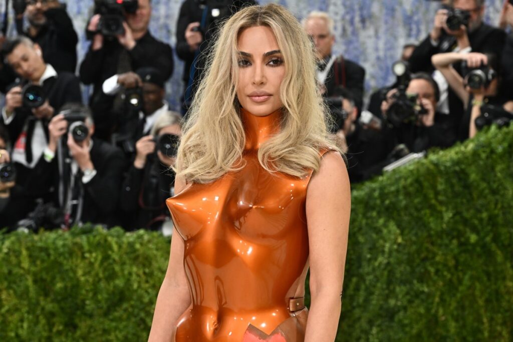 Kim Kardashian sonriendo mientras estudia o se prepara para algo, con un libro o documentos de derecho en la mano