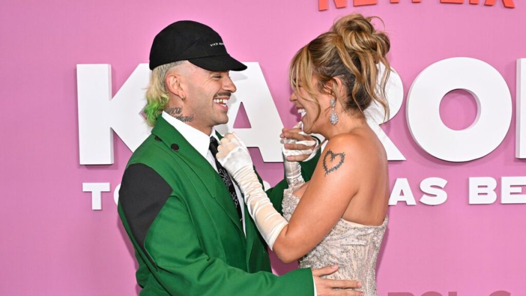 Feid en el escenario con un traje de arriero con detalles verdes, sonriendo y mencionando a Karol G