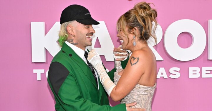 Feid en el escenario con un traje de arriero con detalles verdes, sonriendo y mencionando a Karol G