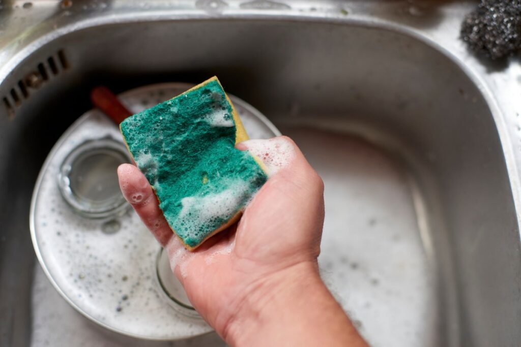 Una persona lavando una esponja en el fregadero con agua y jabón