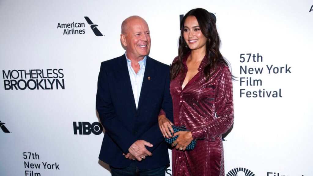 Bruce Willis sonriendo y divirtiéndose en un momento familiar mientras infla un globo