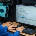 Una persona trabajando en un escritorio con una laptop y código de programación en la pantalla, rodeada de tecnología de vanguardia.