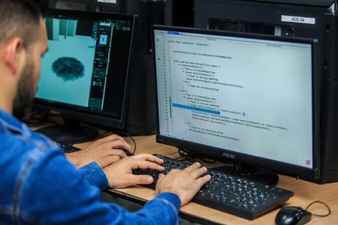 Una persona trabajando en un escritorio con una laptop y código de programación en la pantalla, rodeada de tecnología de vanguardia.