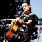 Julieta Venegas cantando en un estadio de fútbol con niñas jugando al fondo