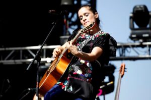 Julieta Venegas cantando en un estadio de fútbol con niñas jugando al fondo