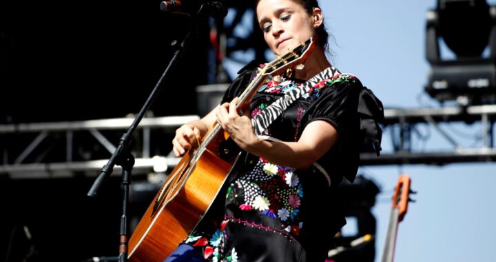 Julieta Venegas cantando en un estadio de fútbol con niñas jugando al fondo