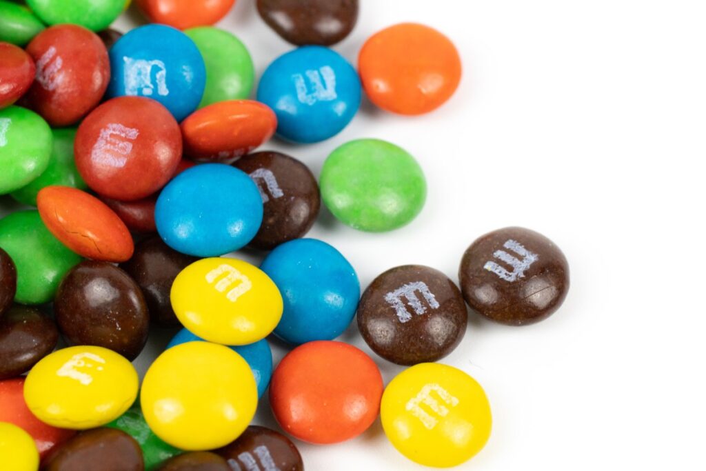 M&M's de colores rojo, verde, amarillo y naranja sobre una superficie blanca