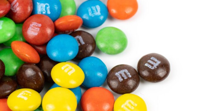 M&M's de colores rojo, verde, amarillo y naranja sobre una superficie blanca
