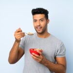 Una mujer con un rostro saludable y atractivo sonriendo mientras come alimentos frescos y naturales.