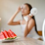 Una sandía y fresas frescas sobre una mesa de madera, rodeadas de agua y hojas verdes