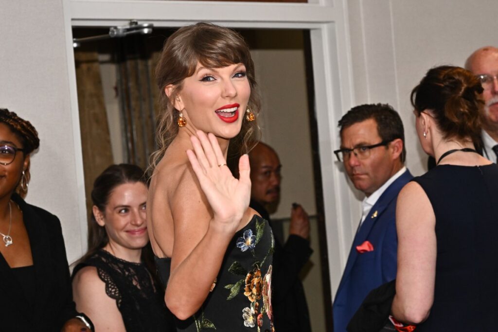 Taylor Swift sonriendo mientras sostiene una guitarra, con un fondo de juguetes de Toy Story