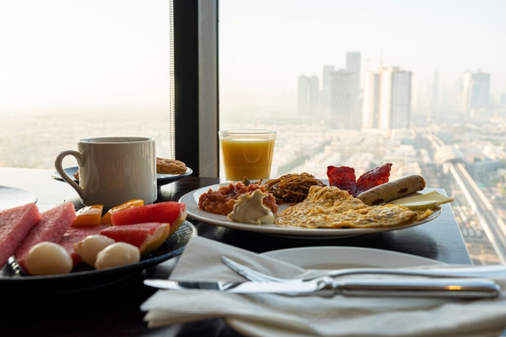 Un desayuno americano con variedad de alimentos, como jugo de naranja, croasanes y huevos revueltos, sobre una mesa de hotel.