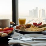 Un desayuno americano con variedad de alimentos, como jugo de naranja, croasanes y huevos revueltos, sobre una mesa de hotel.