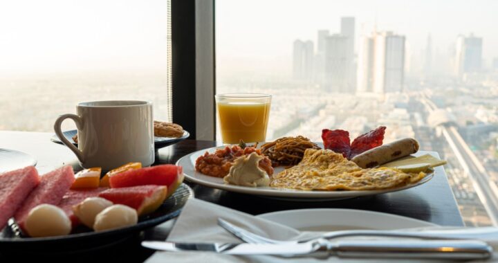 Un desayuno americano con variedad de alimentos, como jugo de naranja, croasanes y huevos revueltos, sobre una mesa de hotel.